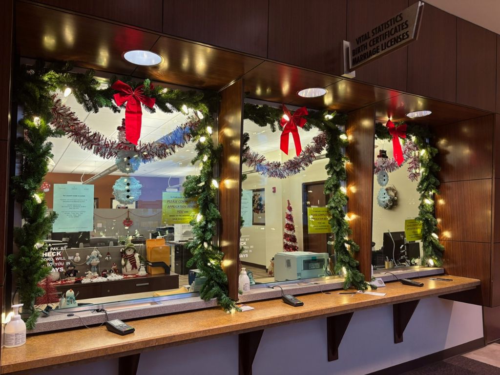 Interior service counter framed with lit evergreen garland and red bows above the transaction windows.