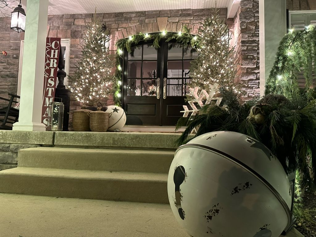 Covered stone porch at night with lit garland over the doors, two lit trees and holiday decorations on the steps.